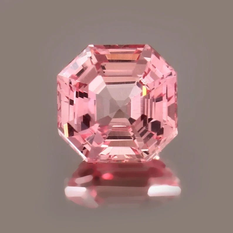Padparadscha Sapphire on a reflective surface with a gray background