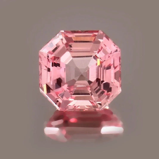 Padparadscha Sapphire on a reflective surface with a gray background