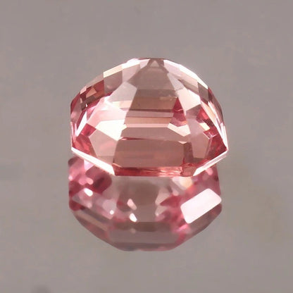 Padparadscha Sapphire on a reflective surface with a gray background