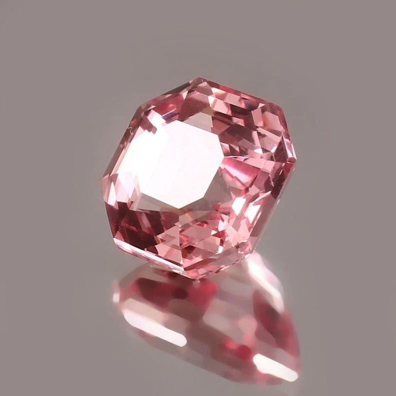 Padparadscha Sapphire on a reflective surface with a gray background