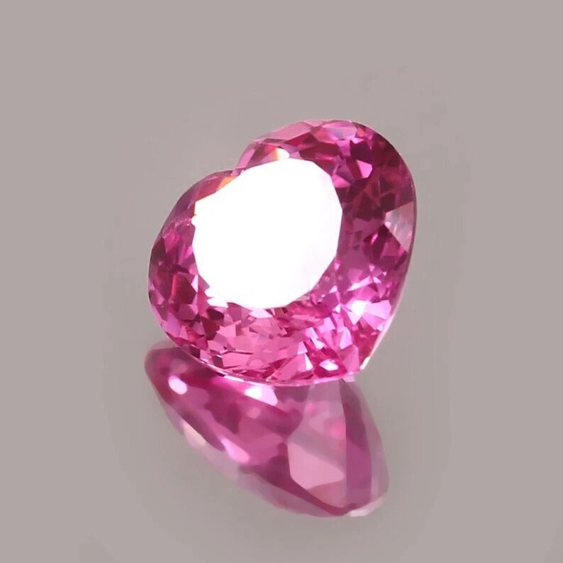 Heart-shaped pink sapphire held by tweezers on a gray background