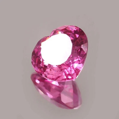 Heart-shaped pink sapphire held by tweezers on a gray background