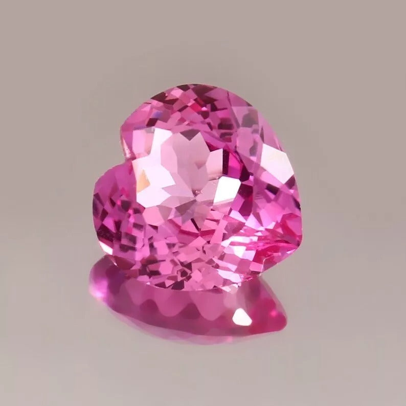 Heart-shaped pink sapphire held by tweezers on a gray background