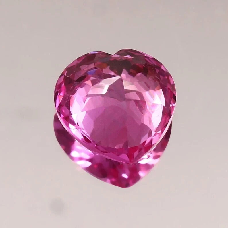 Heart-shaped pink sapphire held by tweezers on a gray background