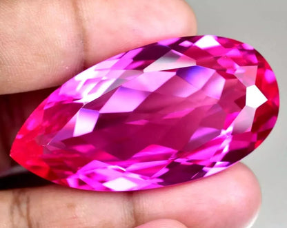 mogok pink ruby pear held between fingers against a neutral background