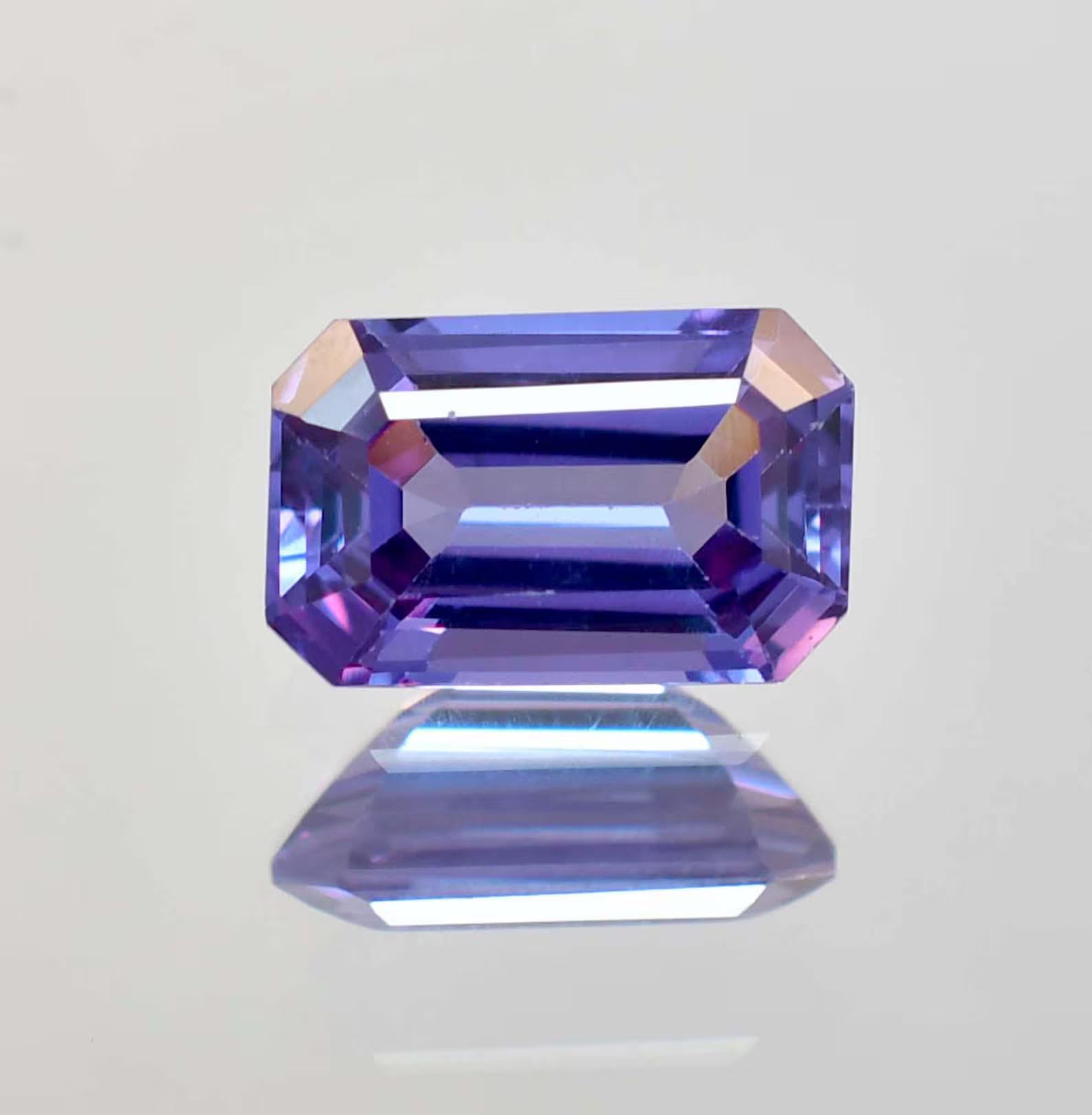 Faceted Alexandrite  gemstone on a reflective surface with a light gray background