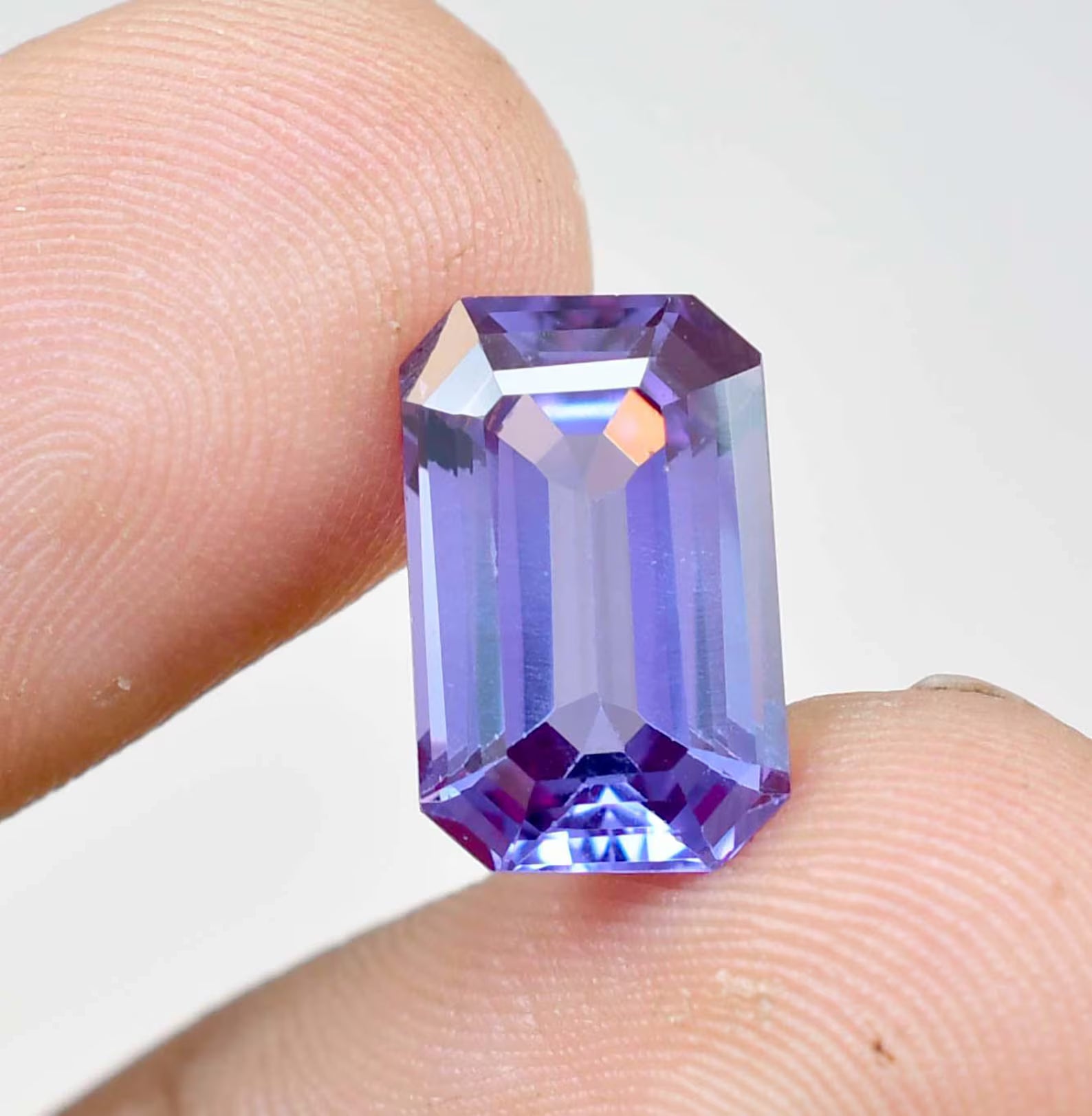 Alexandrite gemstone held between two fingers against a white background