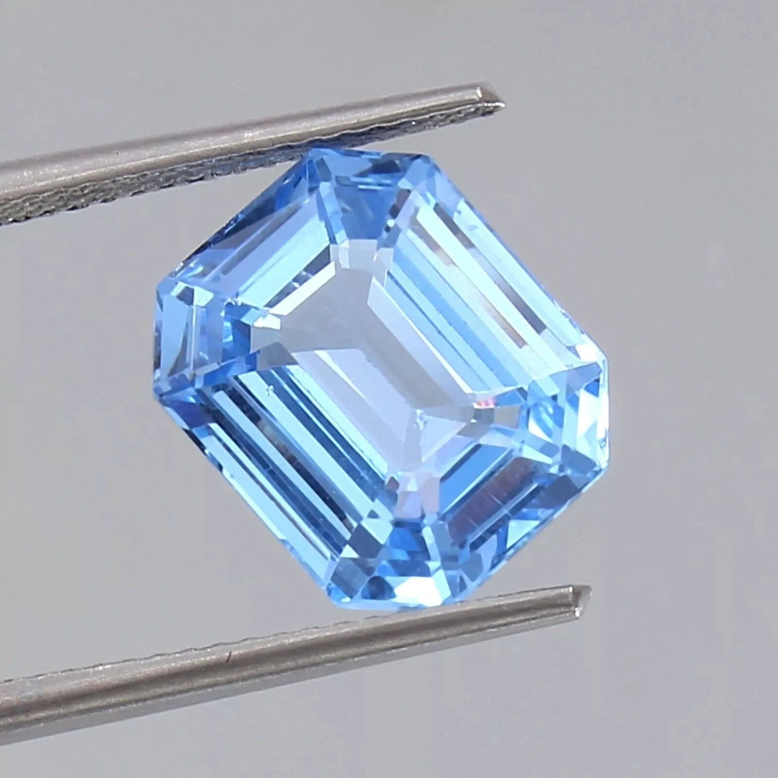 Blue Spinel gemstone held between tweezers on a gray background