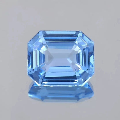 Blue Spinel  gemstone with an emerald cut on a gray background