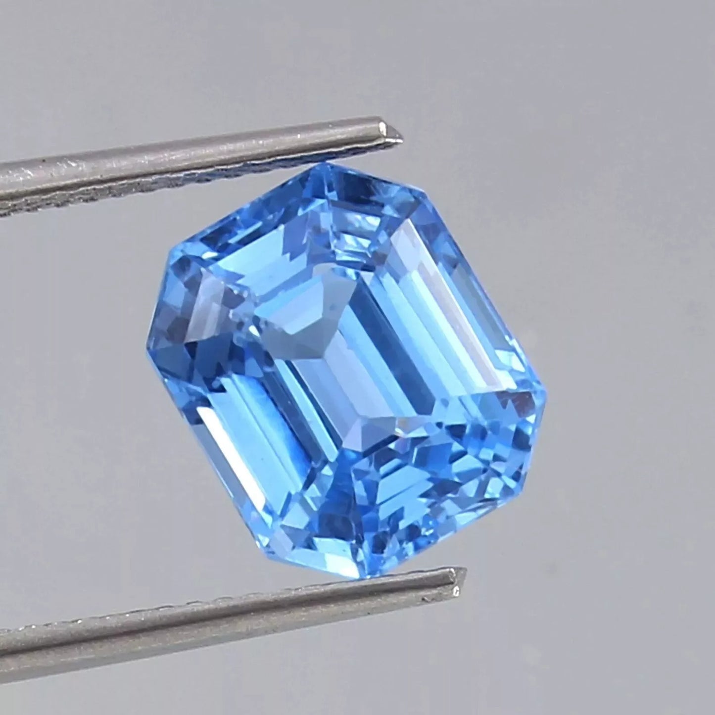 Blue Spinel gemstone held by tweezers against a neutral background