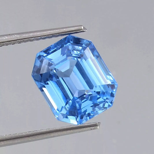 Blue Spinel gemstone held by tweezers against a neutral background