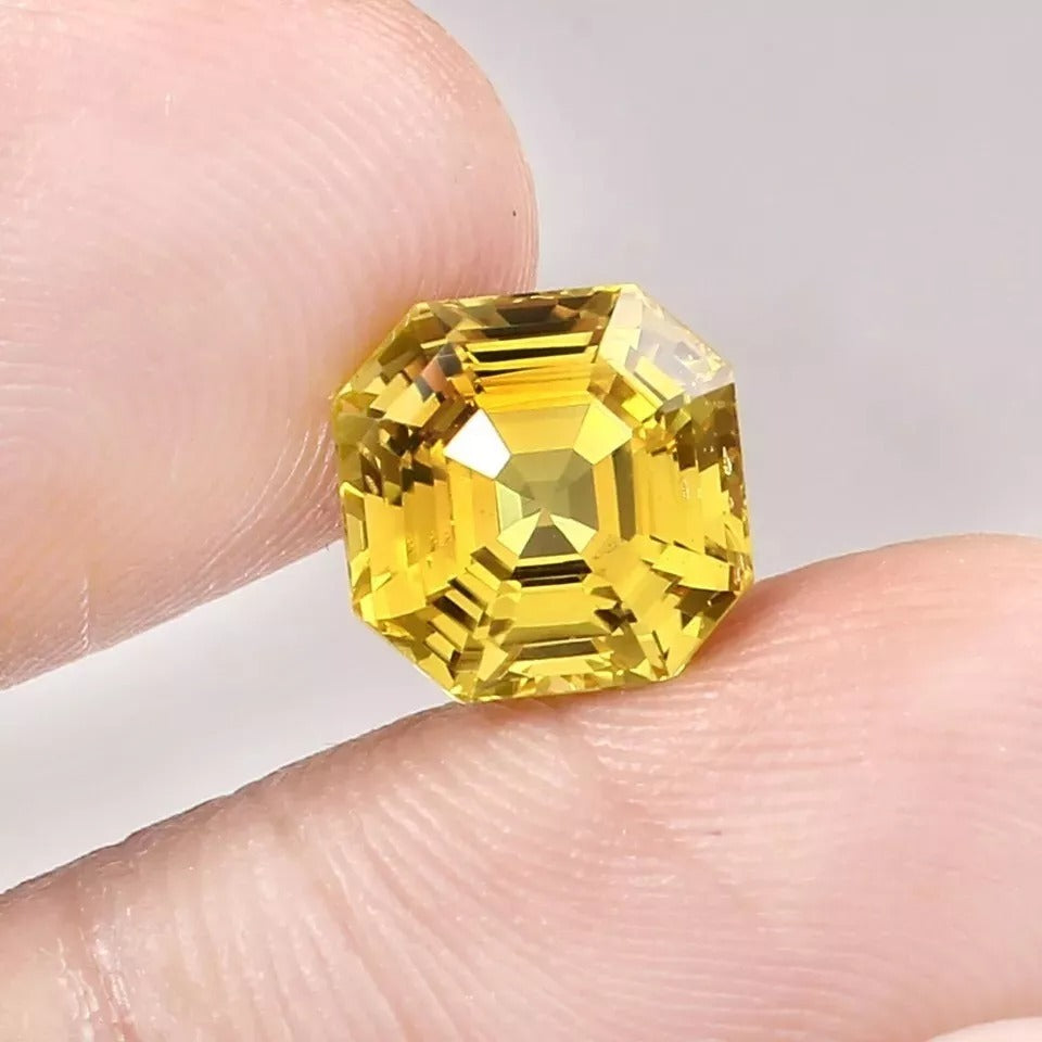 Yellow Sapphire gemstone held between fingers against a neutral background