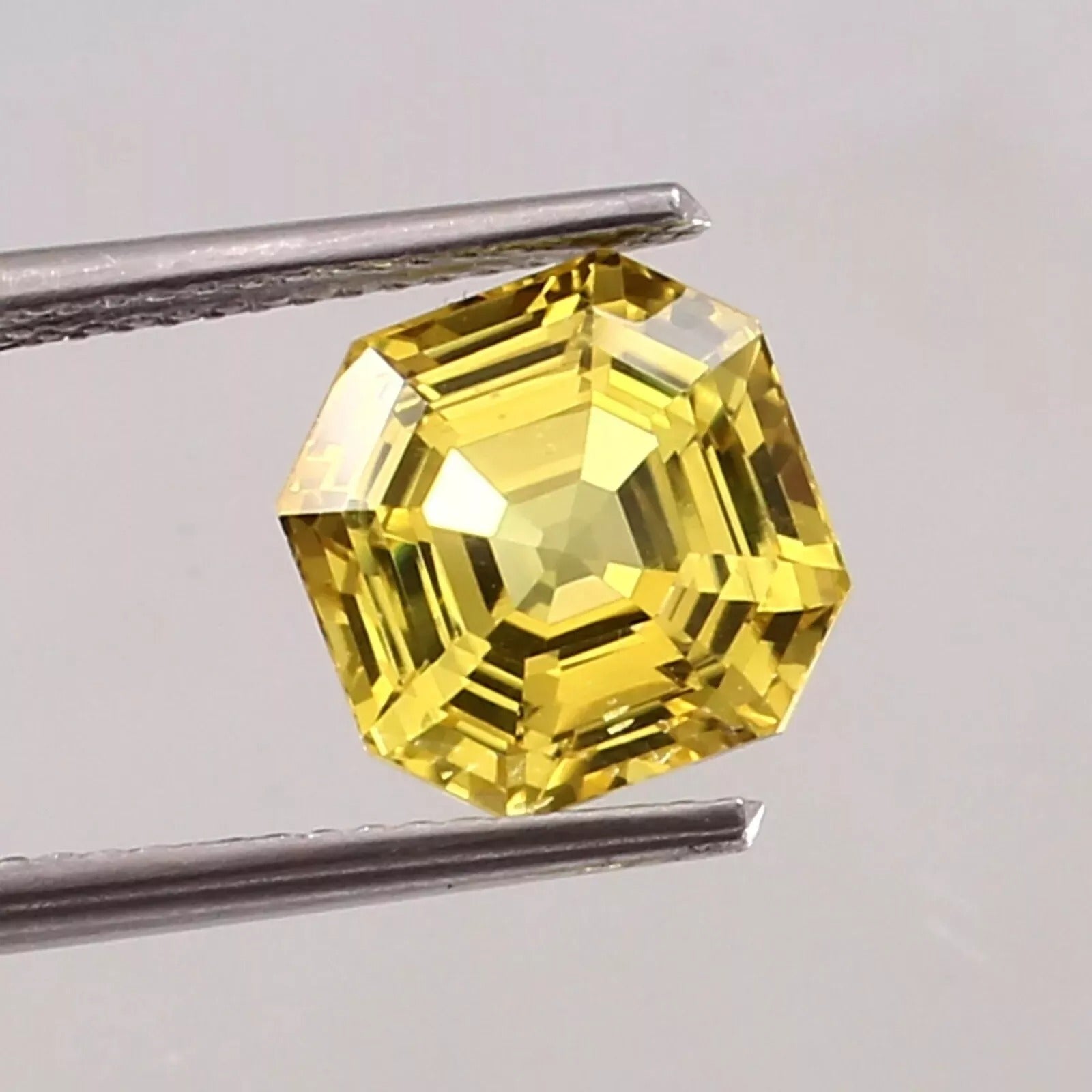 Yellow Sapphire gemstone held by tweezers against a gray background