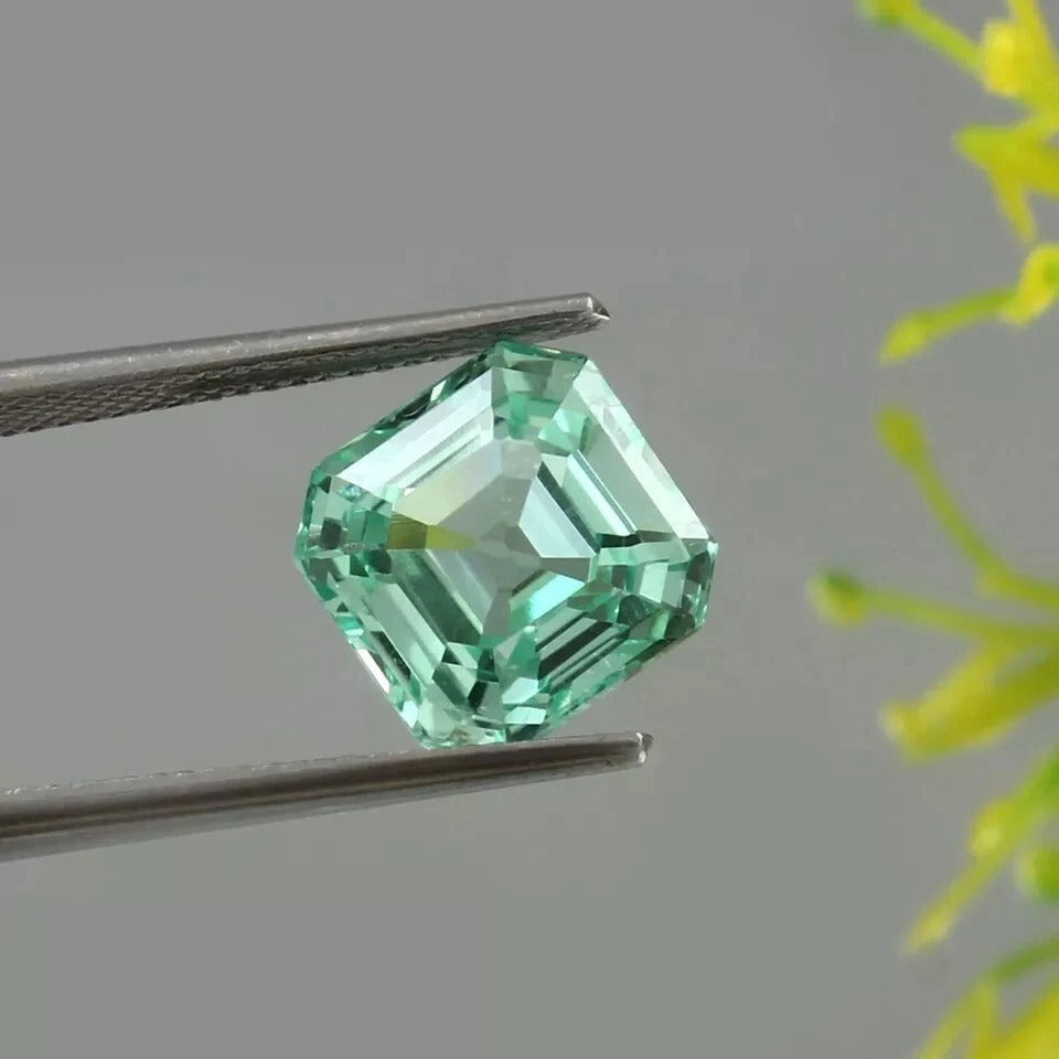 Green Sapphire gemstone held by tweezers against a neutral background