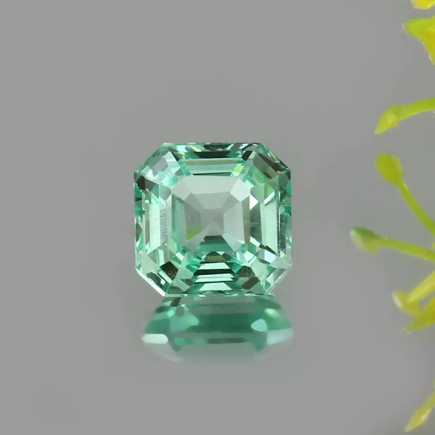 Green Sapphire gemstone on a gray background with a yellow flower in the corner