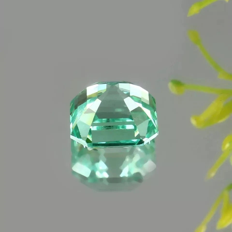 Green Sapphire gemstone on a gray background with a yellow flower