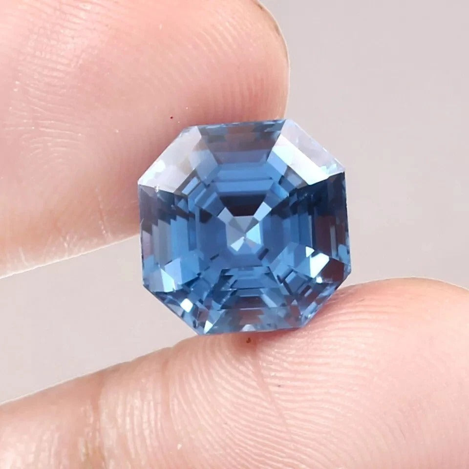 Blue Aquamarine gemstone held between two fingers against a neutral background