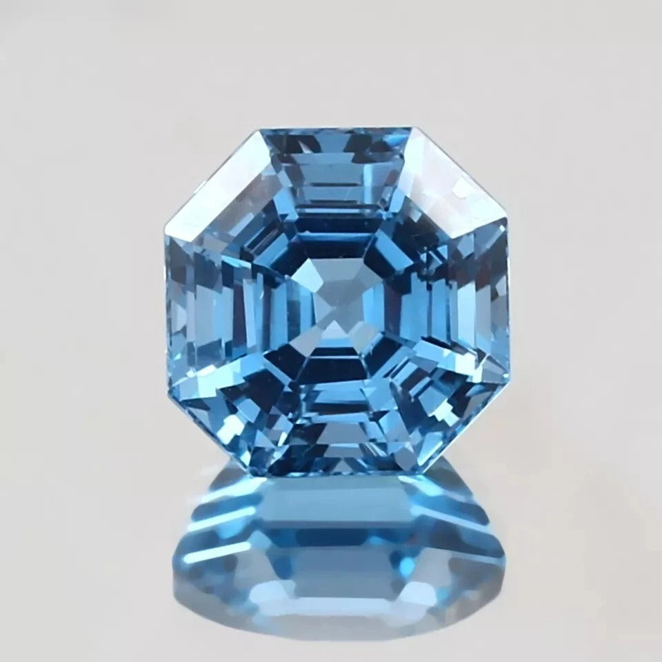 Blue Brazilian Aquamarine gemstone with a hexagonal cut on a light gray background