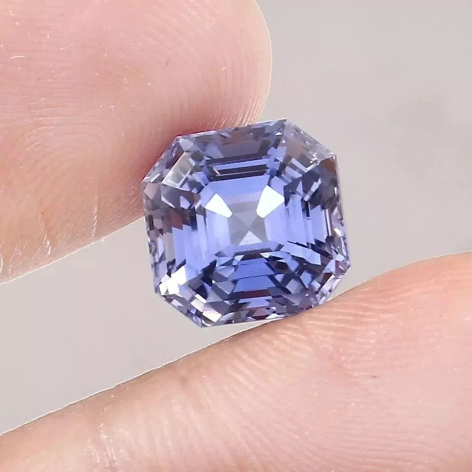 Asscher Blue sapphire gemstone held between fingers against a neutral background