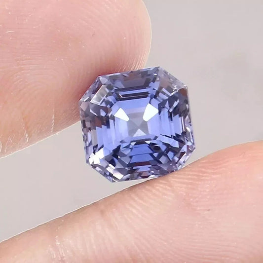 Asscher Blue sapphire gemstone held between fingers against a neutral background