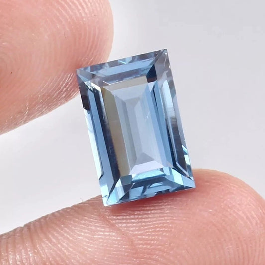 Aquamarine blue gemstone held between fingers against a neutral background