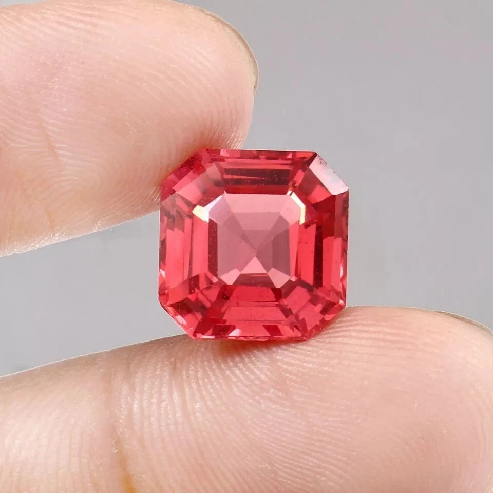 Solomon Color Untreated Padparadscha Sapphire gemstone held between fingers against a neutral background