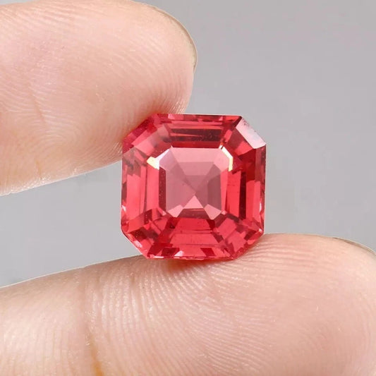 Solomon Color Untreated Padparadscha Sapphire gemstone held between fingers against a neutral background