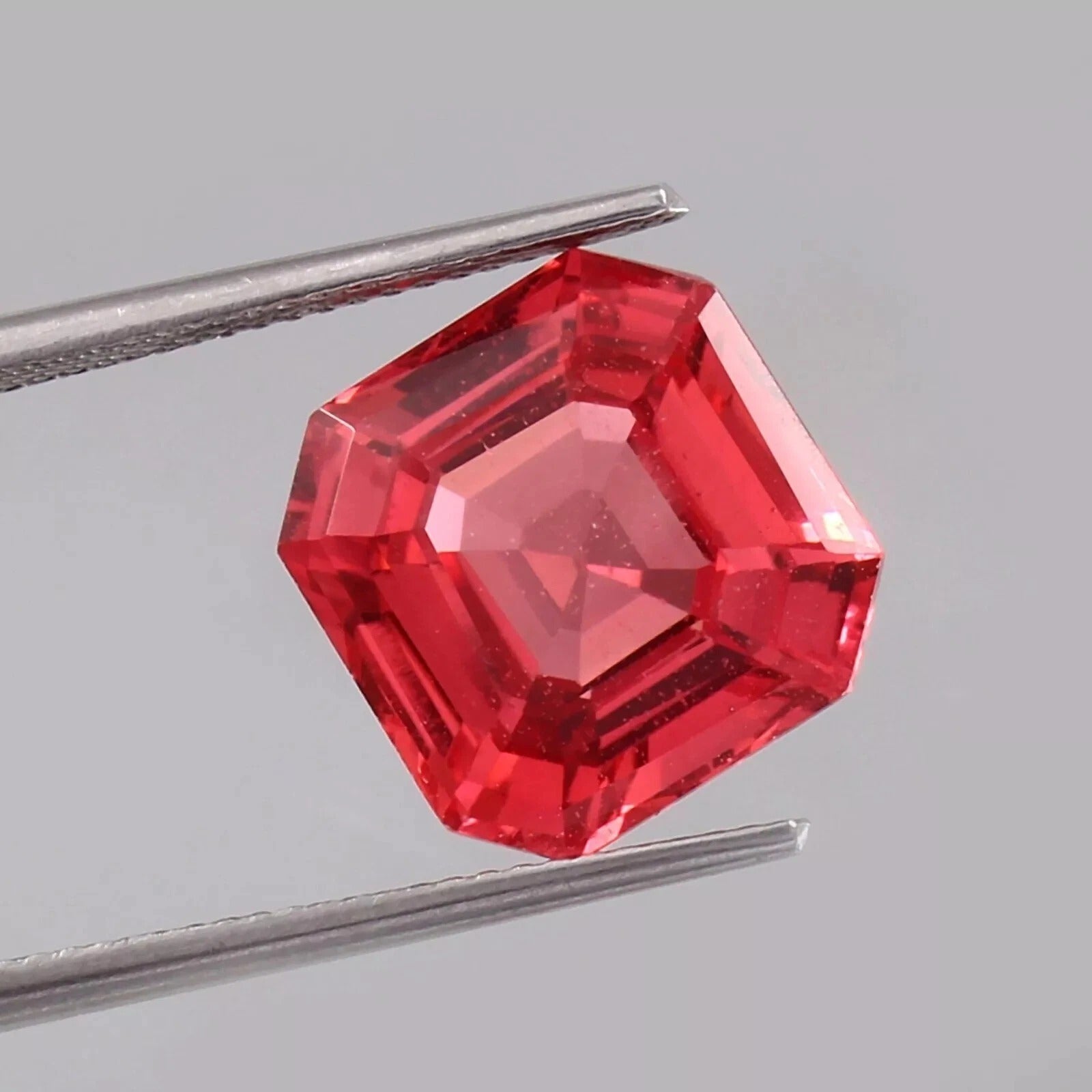 Solomon Color Untreated Padparadscha Sapphire  gemstone held by tweezers on a gray background