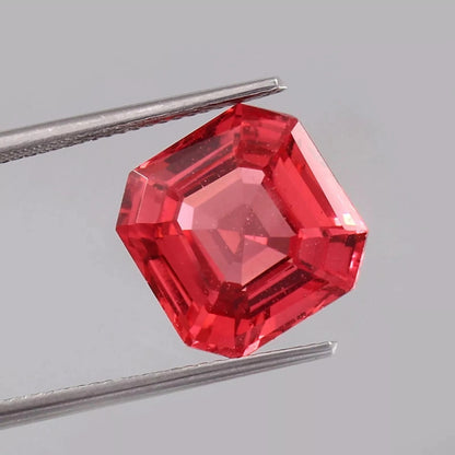 Solomon Color Untreated Padparadscha Sapphire  gemstone held by tweezers on a gray background