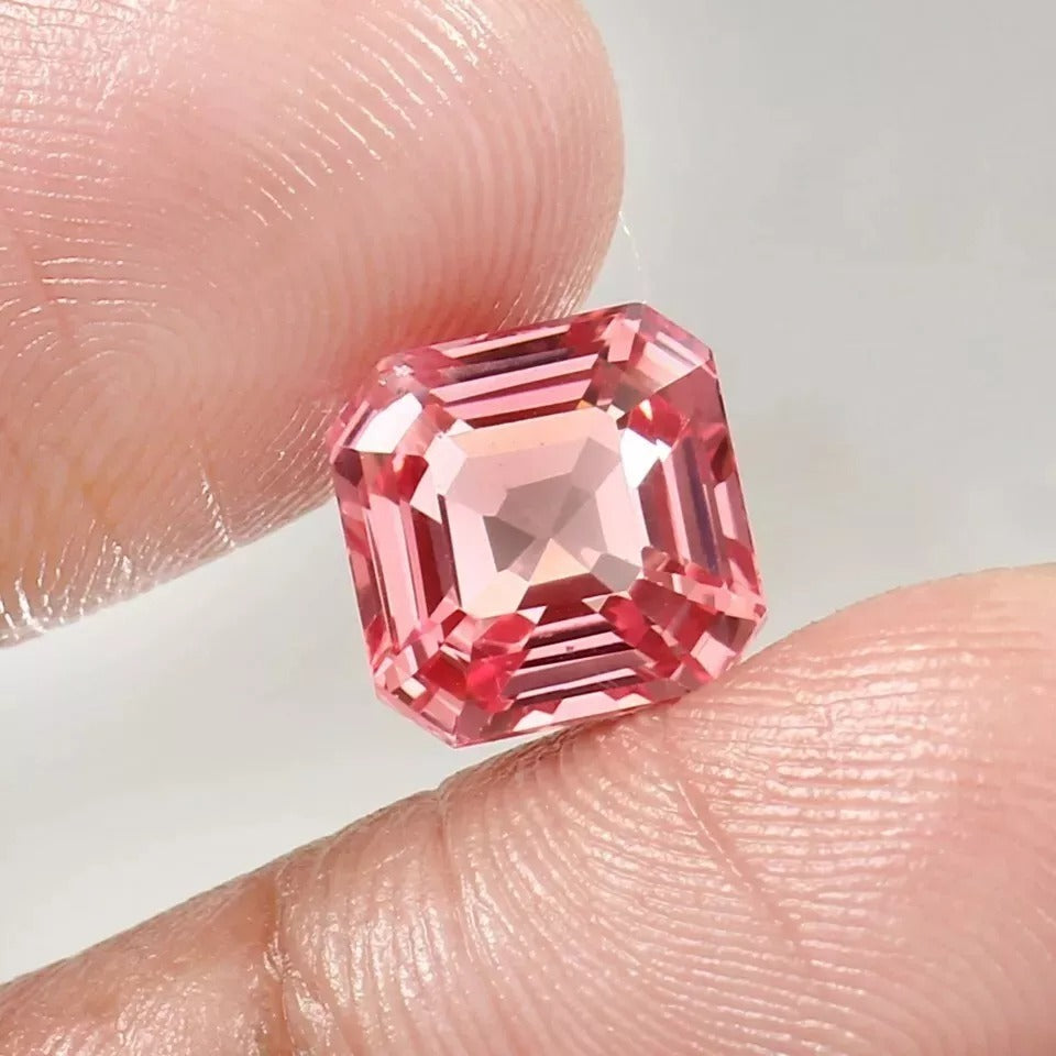 Padparadscha Sapphire gemstone held between fingers against a neutral background