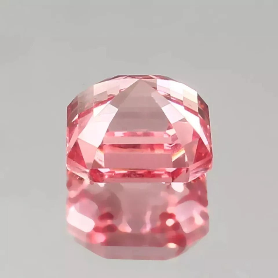 Faceted Padparadscha Sapphire gemstone on a gray background