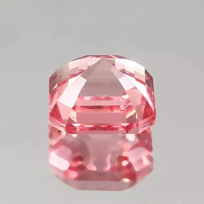 Faceted Padparadscha Sapphire gemstone on a gray background
