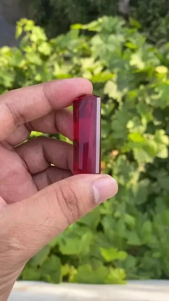 Hand holding a Red huge burma Ruby against a blurred green background