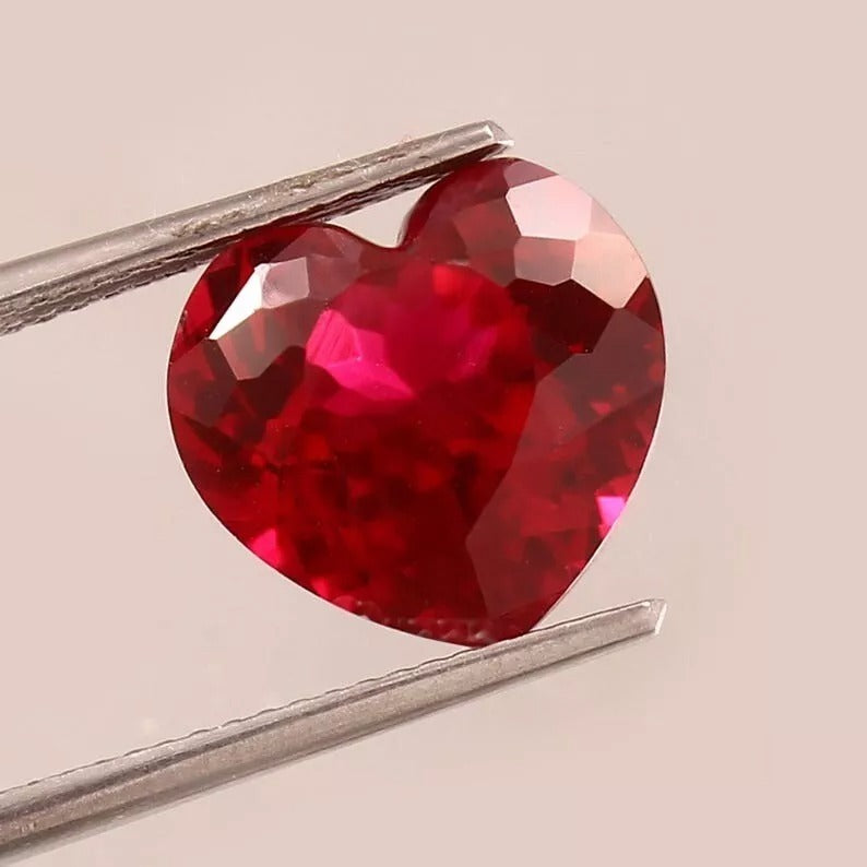 Heart-shaped Unheated Blood Red Mozambique Ruby gemstone held by tweezers on a beige background