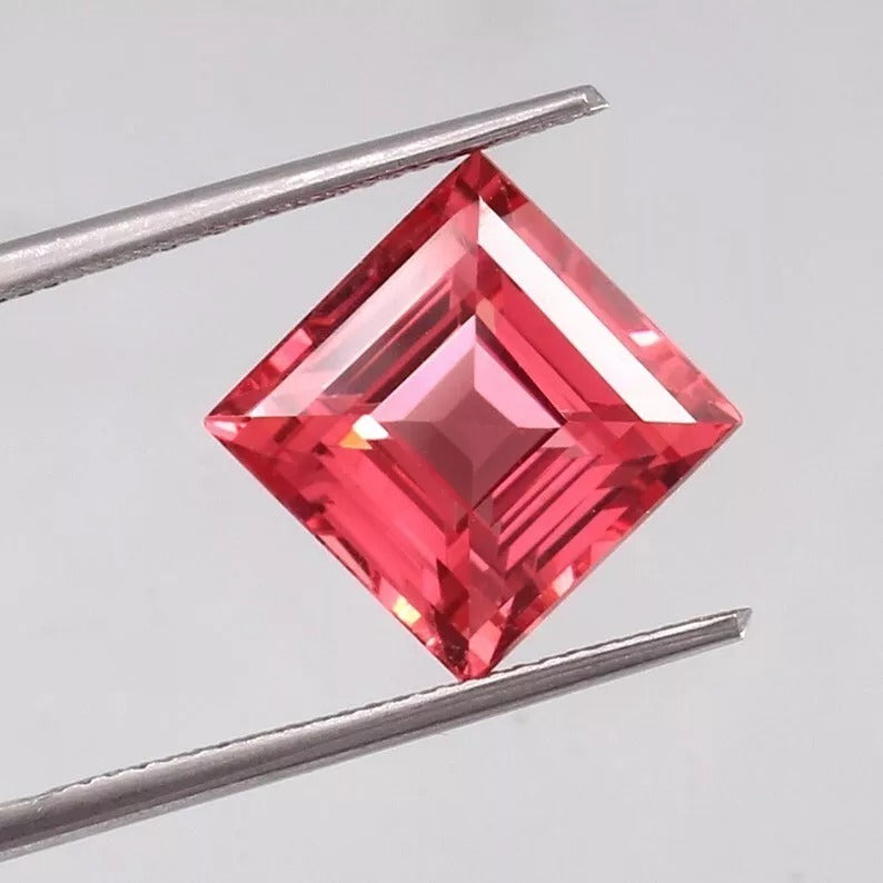Square-cut Solomon Color Ceylon Padparadscha Sapphire gemstone held between tweezers on a light gray background
