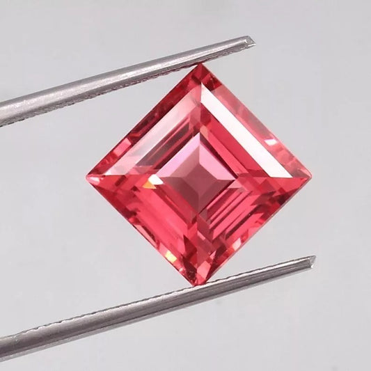 Square-cut Solomon Color Ceylon Padparadscha Sapphire gemstone held between tweezers on a light gray background