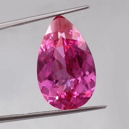 Teardrop-shaped Flawless Ceylon Pink Sapphire gemstone held by tweezers on a light gray background