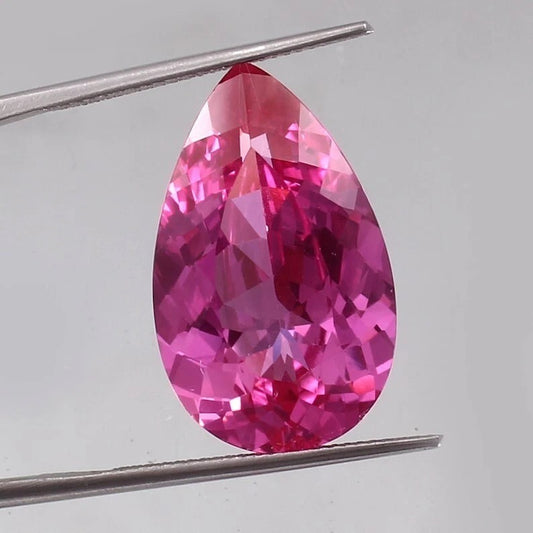 Teardrop-shaped Flawless Ceylon Pink Sapphire gemstone held by tweezers on a light gray background
