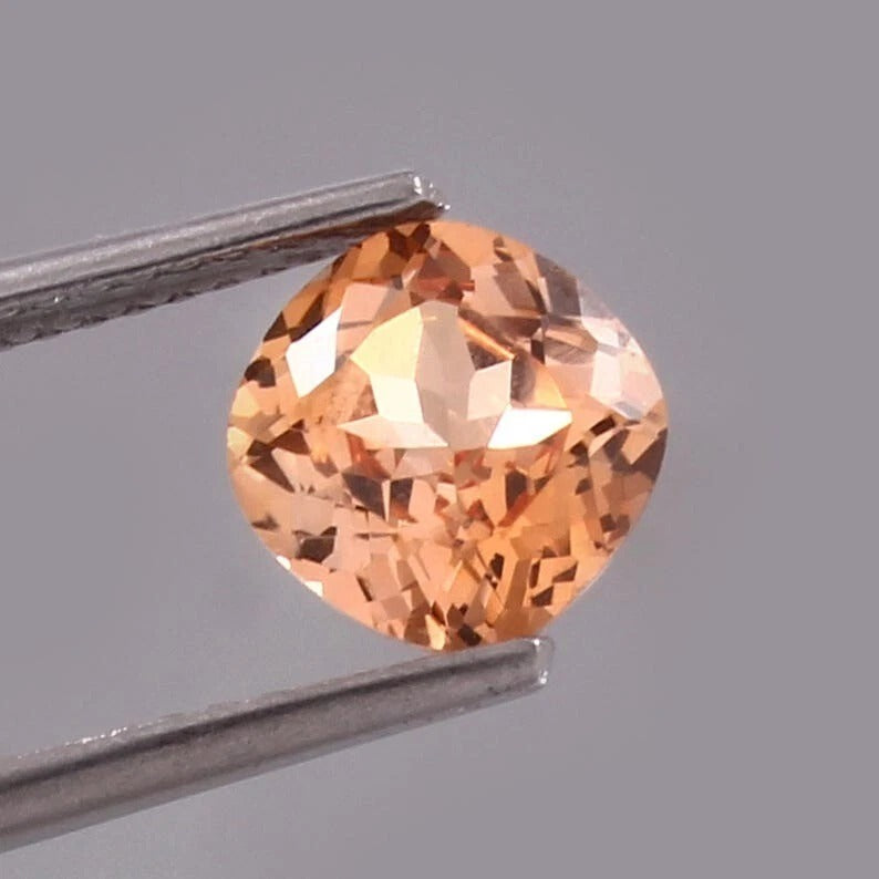 Padparadscha Sapphire – Peach to Orange gemstone held by tweezers against a gray background