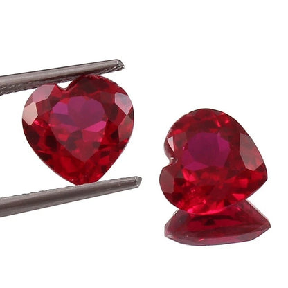 Pair Blood Red Mozambique Ruby heart-shaped gemstones held by tweezers on a white background