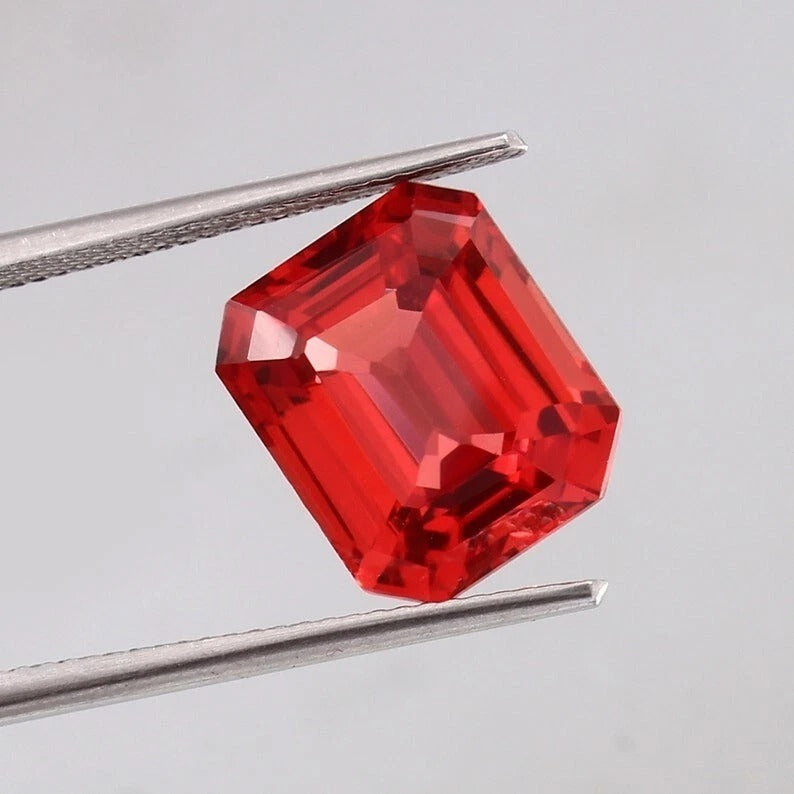 Solomon Color Padparadscha Sapphire gemstone held between tweezers against a gray background