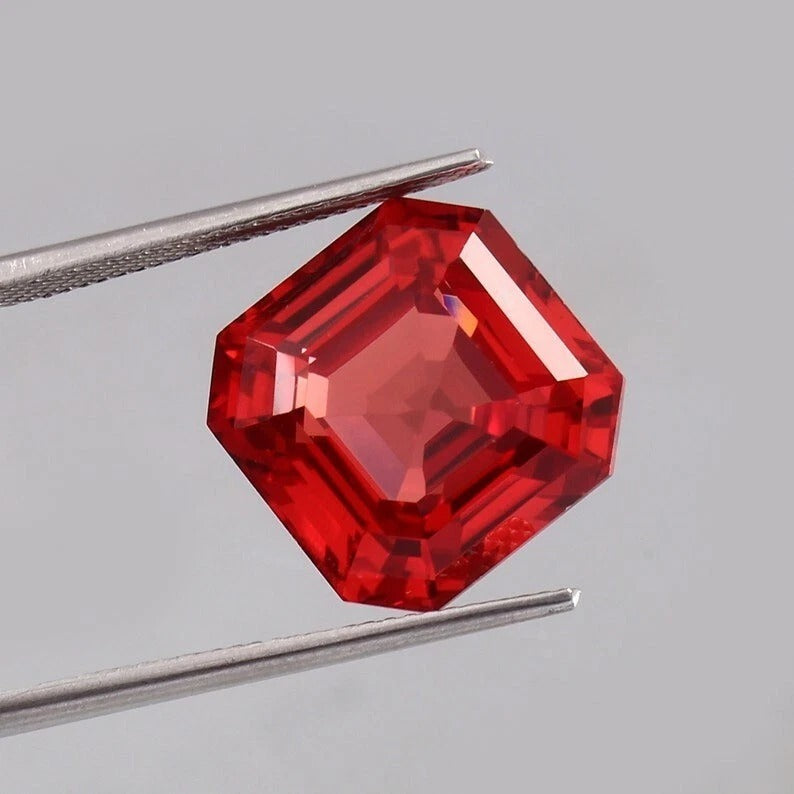 Solomon Padparadscha Sapphire gemstone held by tweezers against a gray background