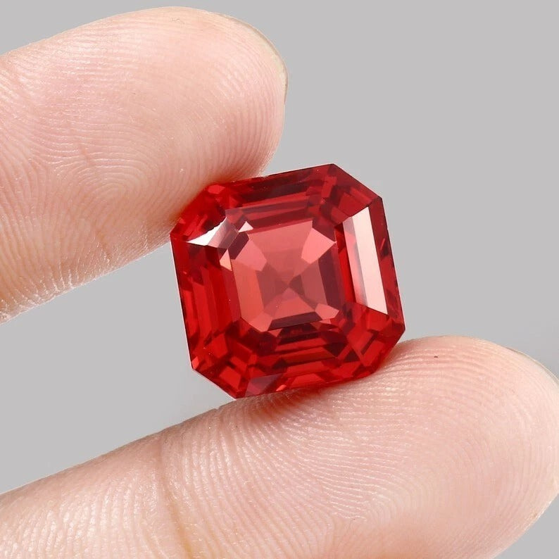 Solomon Padparadscha Sapphire gemstone held between fingers against a gray background
