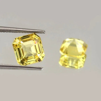 Yellow Ceylon Sapphire Pair gemstones held by tweezers on a gray background