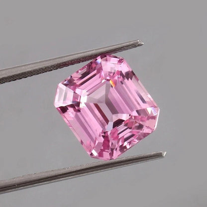 Pink Morganite Madagascar gemstone held between tweezers against a gray background