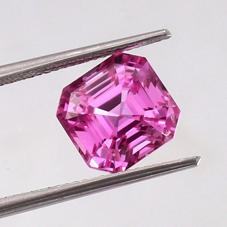 Pink Sapphire Loose Asscher Unheated gemstone held between tweezers on a light gray background