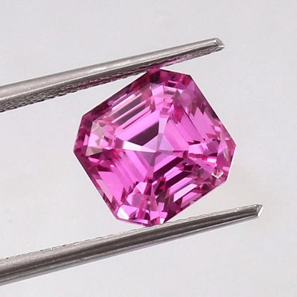 Pink Sapphire Loose Asscher Unheated gemstone held between tweezers on a light gray background