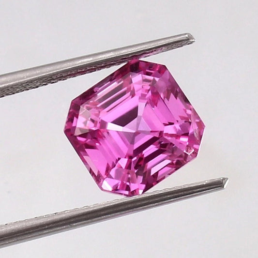 Pink Sapphire Loose Asscher Unheated gemstone held between tweezers on a light gray background