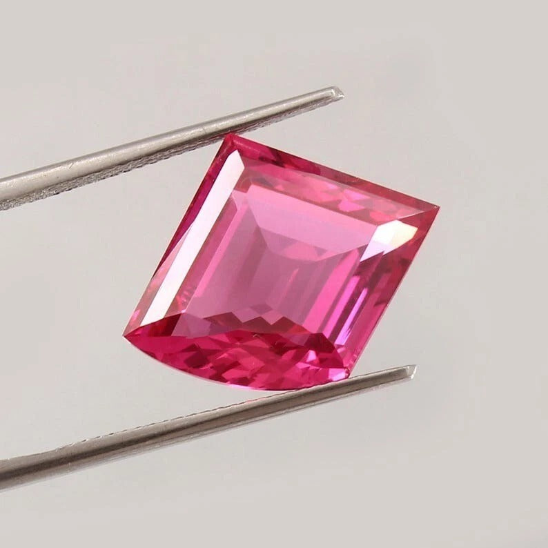 Pink Sapphire Fancy Cut gemstone held by tweezers on a light gray background