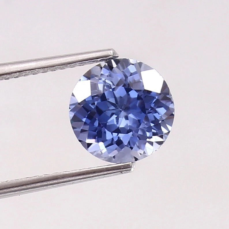 Paste Blue Color Sapphire gemstone held by tweezers on a light gray background